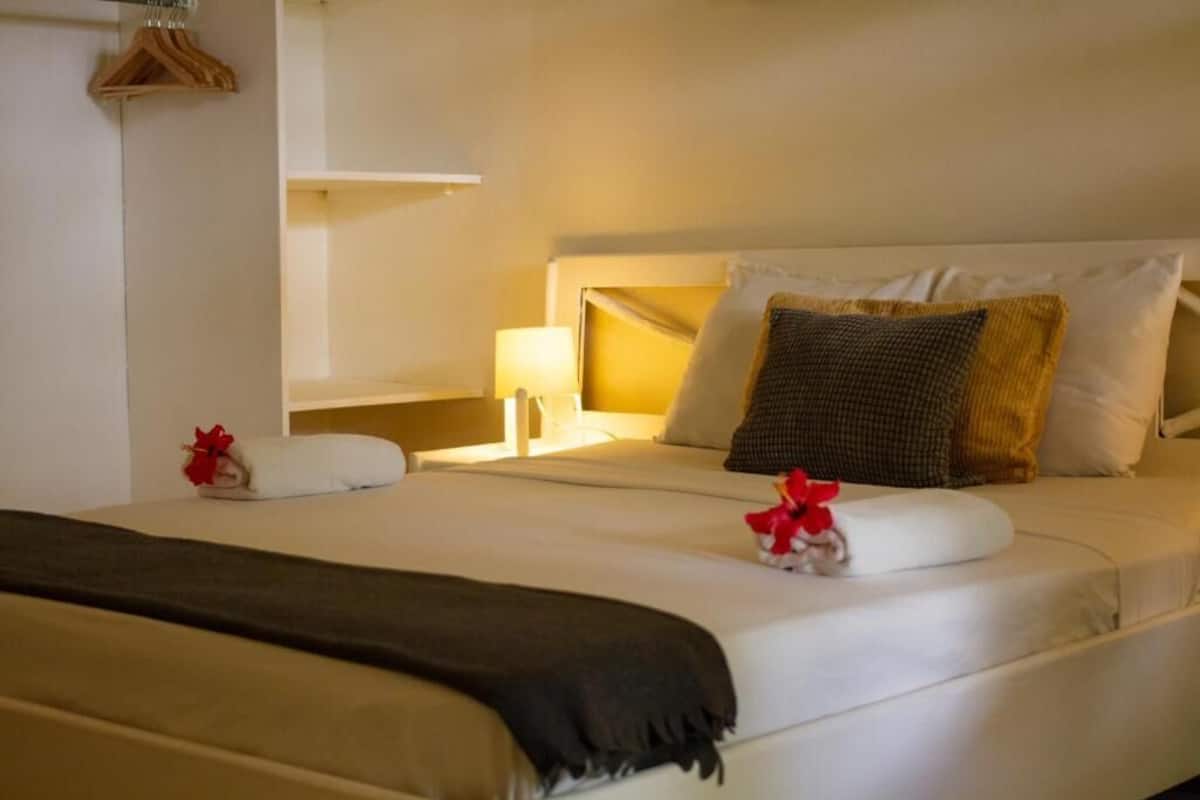 Habitación de hotel con cama, mesita de noche, lámpara y un perchero de madera colgante.