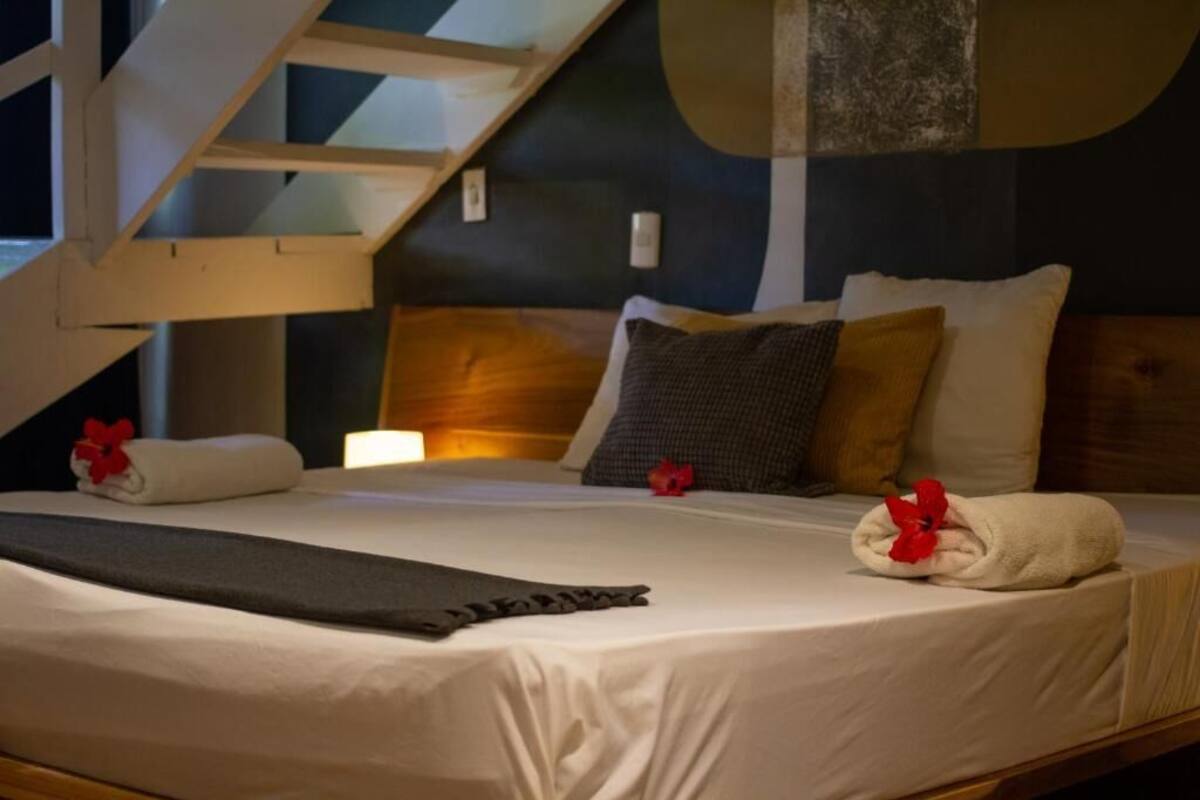 Una habitación de hotel con una cama, almohadas, una colcha y una escalera.