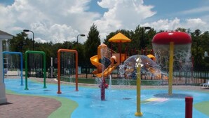 Ein Wasserpark mit Rutschen und Sprudlern, umgeben von einem Pflasterweg.