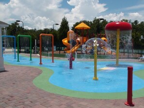 Ein Wasserpark mit Rutschen und Sprudlern, umgeben von einem Pflasterweg.