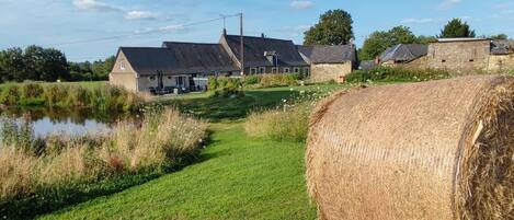 A rural landscape with a pond, hay bales, and stone buildings.