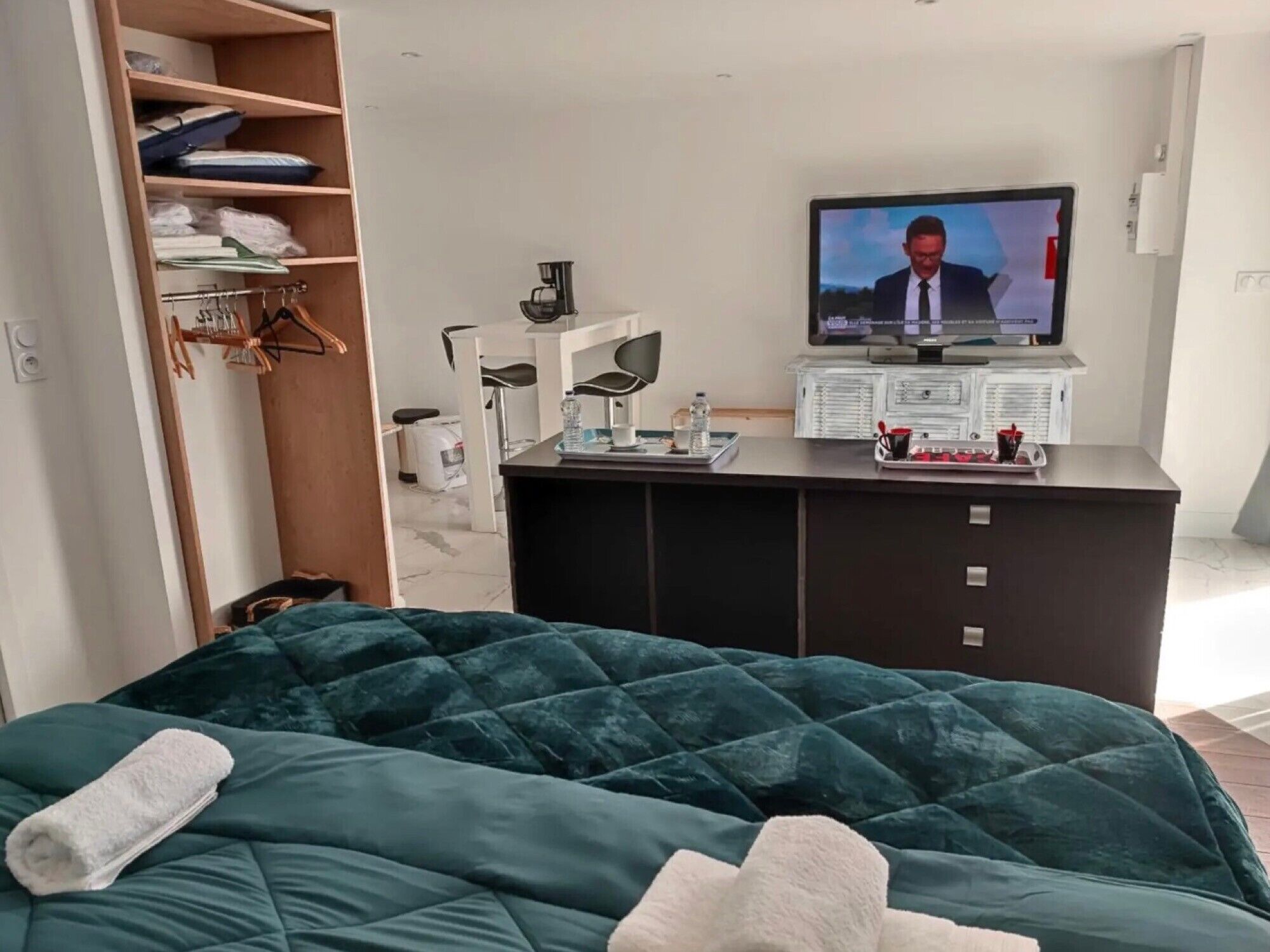 A hotel room with a bed, a TV, a desk with a tray of items, a wardrobe, and a mirror.