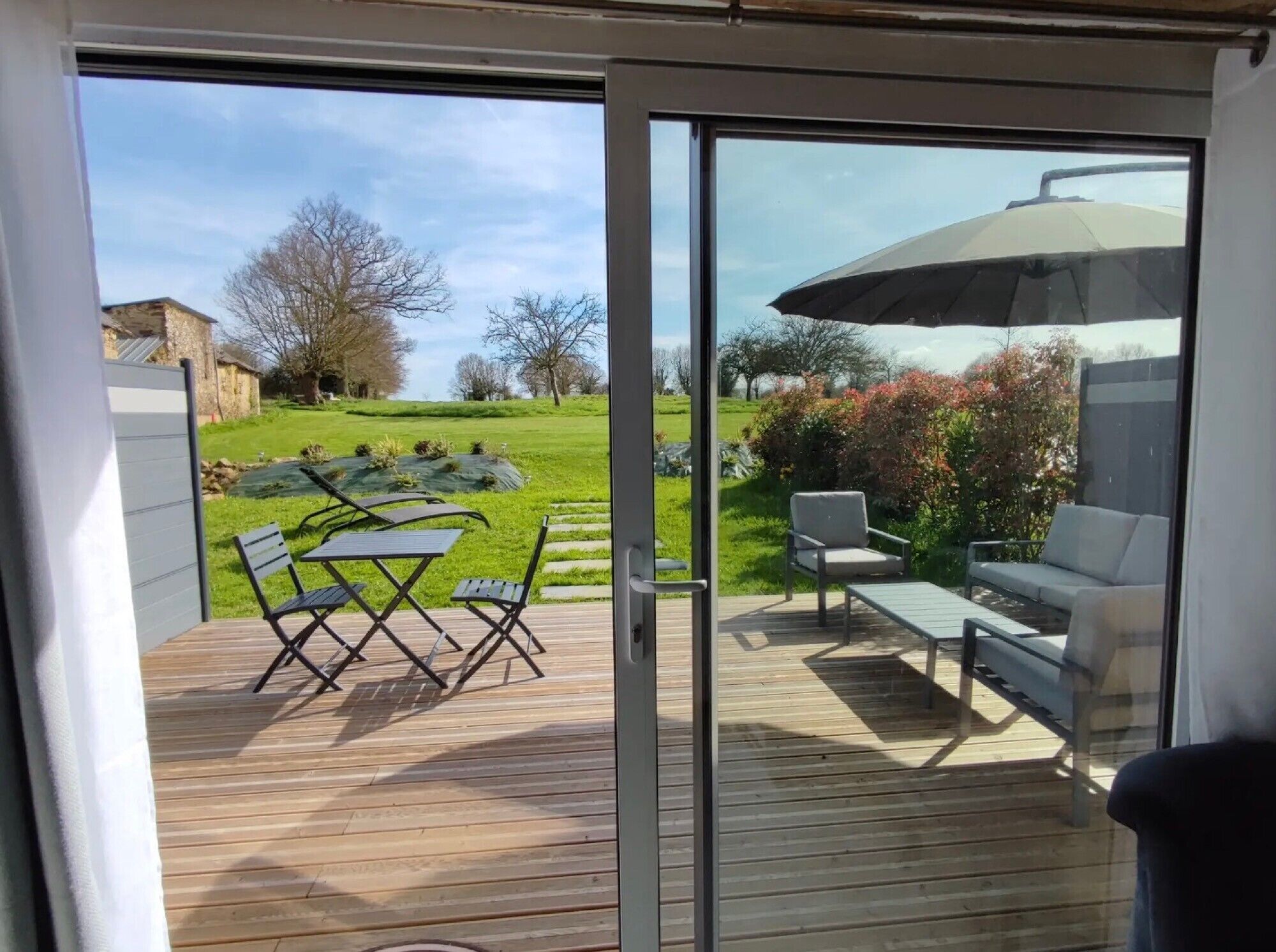 Una terraza con mobiliario exterior, una puerta de cristal y vista a un jardín cubierto de césped.