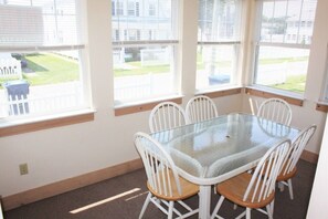 A dining area with a glass table and white chairs, large windows, and a view of a fenced yard. - 66n Gorton Avenue, Old Lyme, CT (Old Lyme)