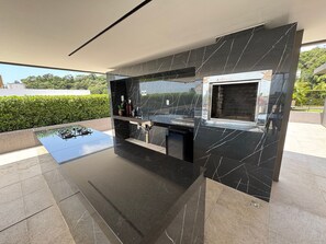 Une cuisine extérieure moderne avec un dosseret en marbre noir, un évier intégré et une fenêtre donnant sur un paysage verdoyant.