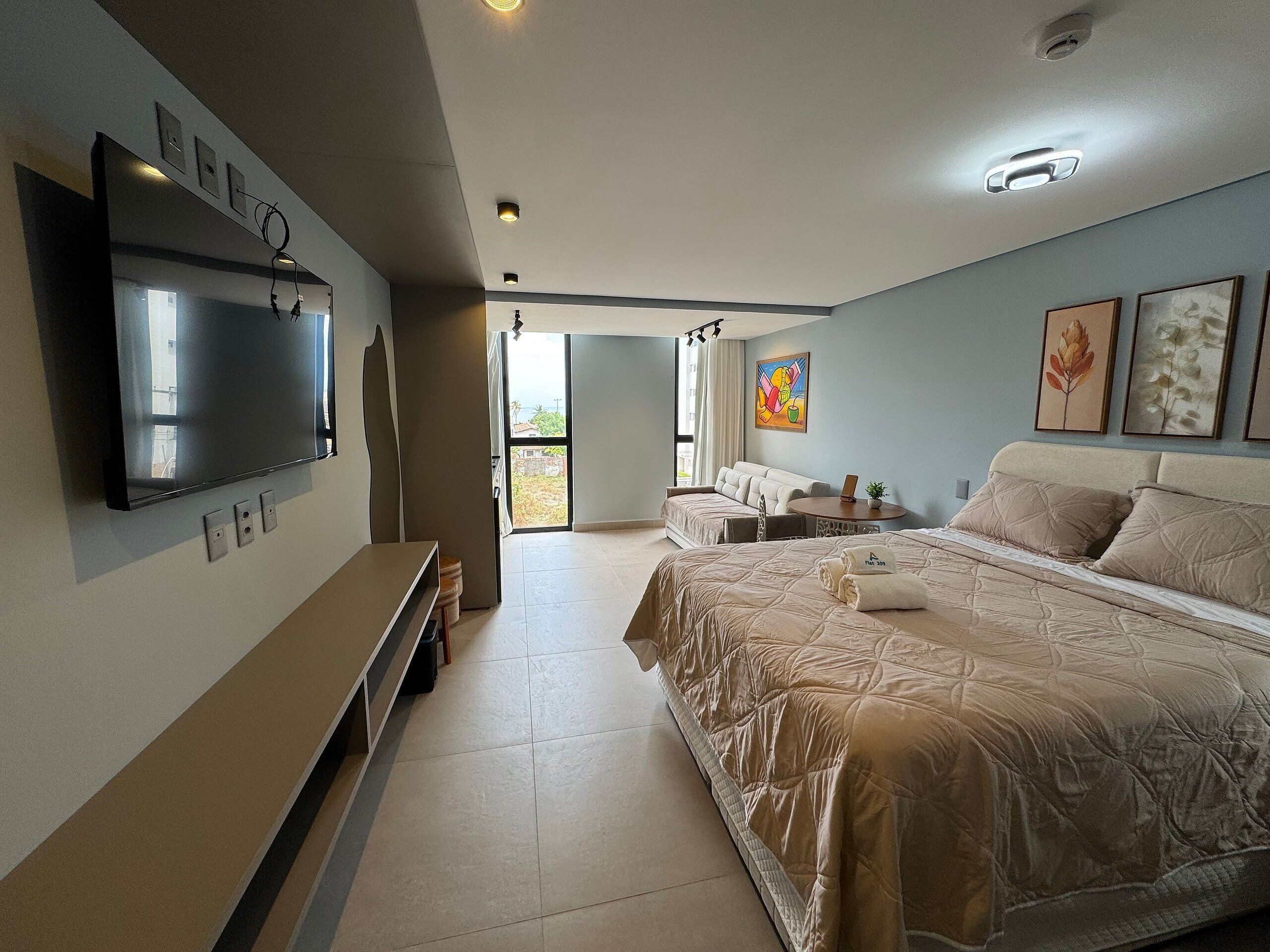 A hotel room with a bed, a TV, a desk, and a window.