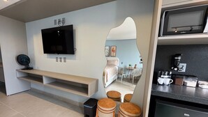 Une cuisine moderne équipée d’un four à micro-ondes, d’une machine à café et de placards. Un téléviseur est fixé au mur, et il y a une petite table avec des chaises.