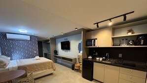 Une chambre d’hôtel moderne équipée d’un lit, d’un canapé, d’une petite table à manger, d’un coin cuisine avec un four à micro-ondes et d’un téléviseur fixé au mur.