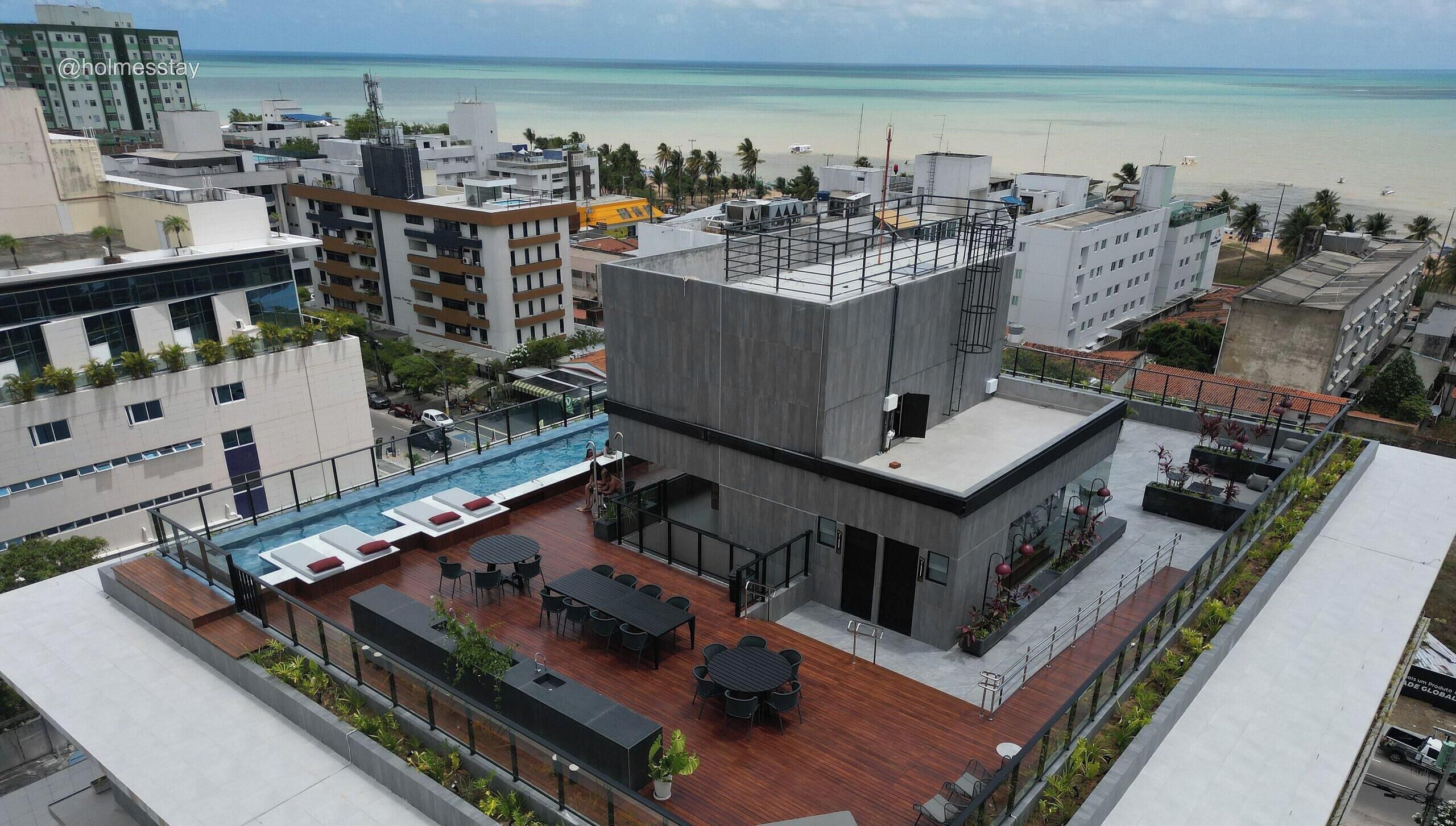 A rooftop pool area with lounge chairs and a dining table, overlooking a beach.