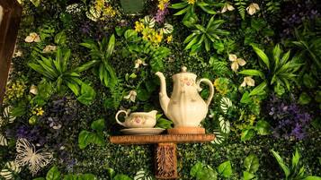 Un mur orné de différentes plantes et fleurs, une petite table avec une théière et une tasse, et un papillon décoratif.