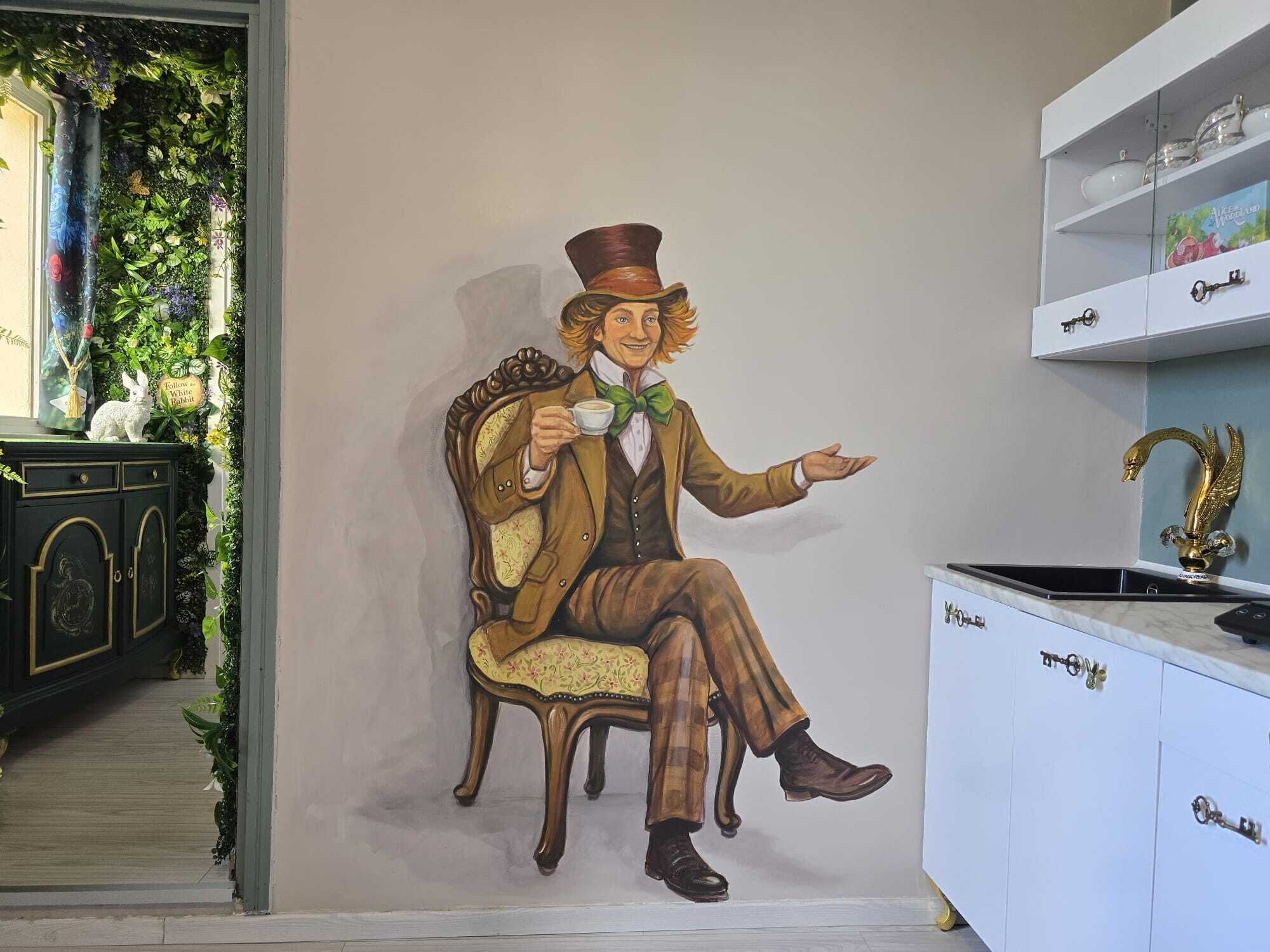 Une fresque murale représentant une figure assise, un meuble avec des clés et une étagère ornée d’objets décoratifs.