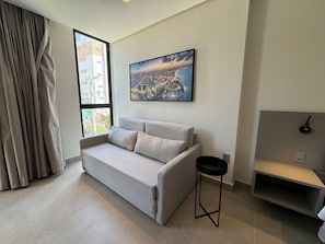 Ein modernes Wohnzimmer mit einer Couch, einem kleinen schwarzen Hocker, einem Stadtbildgemälde und einem Fenster mit Vorhängen.