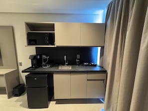Eine kleine Küche mit Spüle, Kaffeemaschine, Mikrowelle und Kühlschrank.
