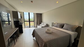 Quarto de hotel moderno com uma cama grande, uma escrivaninha com cadeira, um sofá e uma varanda com vista.