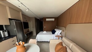 Quarto compacto com cama, sofá, uma mesinha e cozinha compacta.
