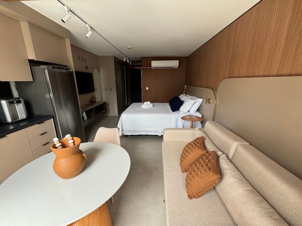 Quarto compacto com cama, sofá, uma mesinha e cozinha compacta.