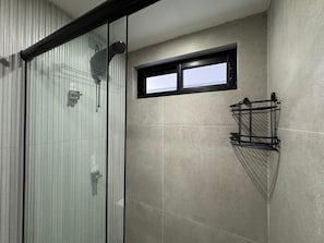 Ein modernes Badezimmer mit Duschkabine aus Glas, einem kleinen Fenster und einem schwarzen Handtuchhalter.