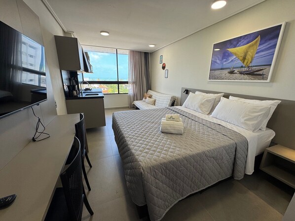 Ein Hotelzimmer mit Bett, Schreibtisch, Fernseher, einem Gemälde und Blick aufs Meer.