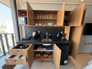 Una cocina compacta con armarios de madera, un lavamanos empotrado y un refrigerador pequeño.