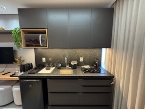 Cozinha moderna com armários escuros, micro-ondas embutido e máquina de café.