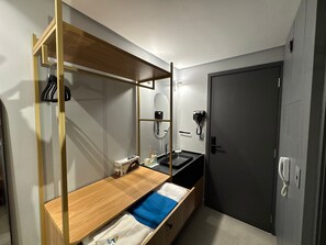 Ein kleines Hotelzimmer mit einem Holzbett, einem kleinen Waschbecken, einem Spiegel, einer Tür und einem Telefon.