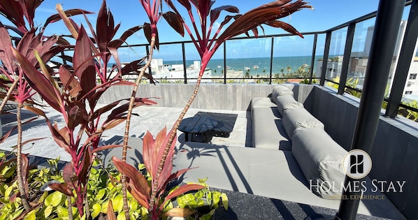 Eine Dachterrasse mit Sitzgelegenheit und Blick auf das Meer, sowie das Logo von Holmes Stay.