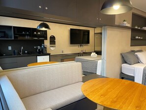 Eine moderne Küchenzeile mit Flachbildfernseher, kleinem Kühlschrank und einer Kaffeemaschine.