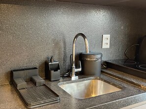 Eine Küche mit einer Edelstahl-Spüle, einem Wasserhahn, einem Wasserkocher und einer Kaffeemaschine.