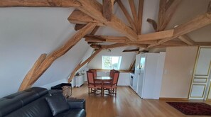 Un loft con vigas de madera a la vista, una zona de comedor con mesa y sillas, un sofá de cuero negro y un refrigerador.