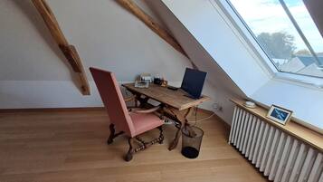 A room with a sloped ceiling, a wooden desk with a laptop, a red chair, and a radiator.