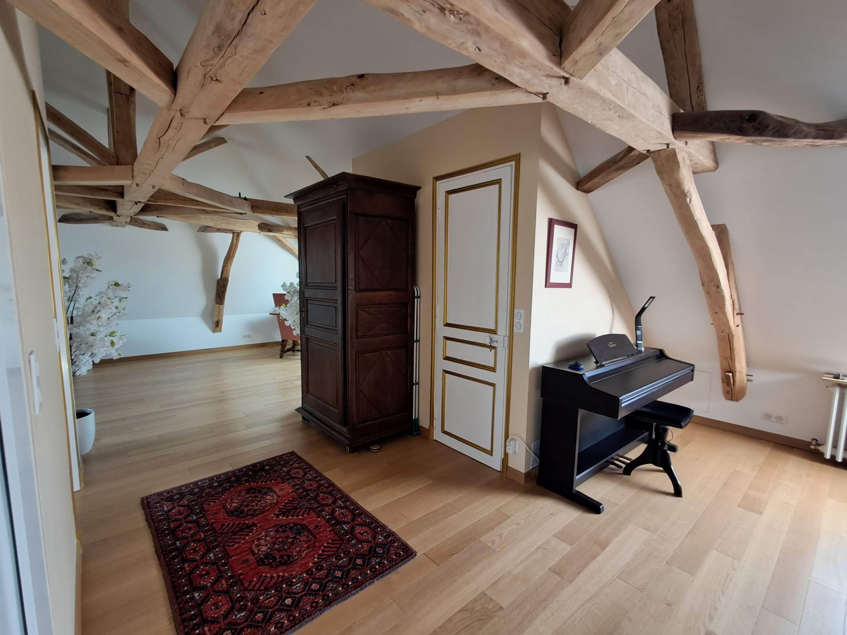 A room with wooden beams, a piano, a cabinet, and a patterned rug.