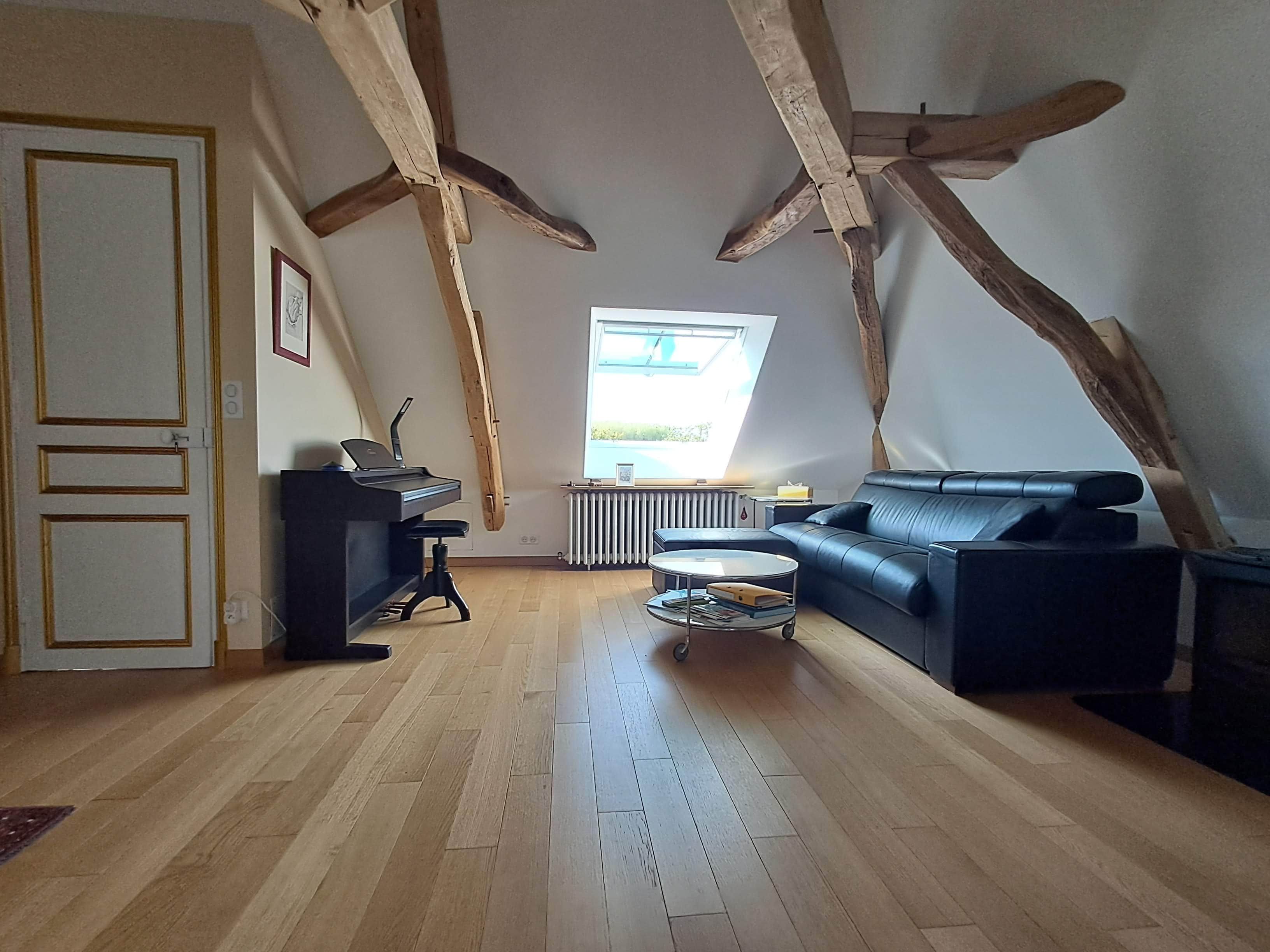 A loft-style room with exposed wooden beams, a piano, a sofa, and a radiator.