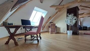 Un dormitorio en el ático con vigas de madera, un escritorio con una computadora, una silla roja y una planta en maceta.