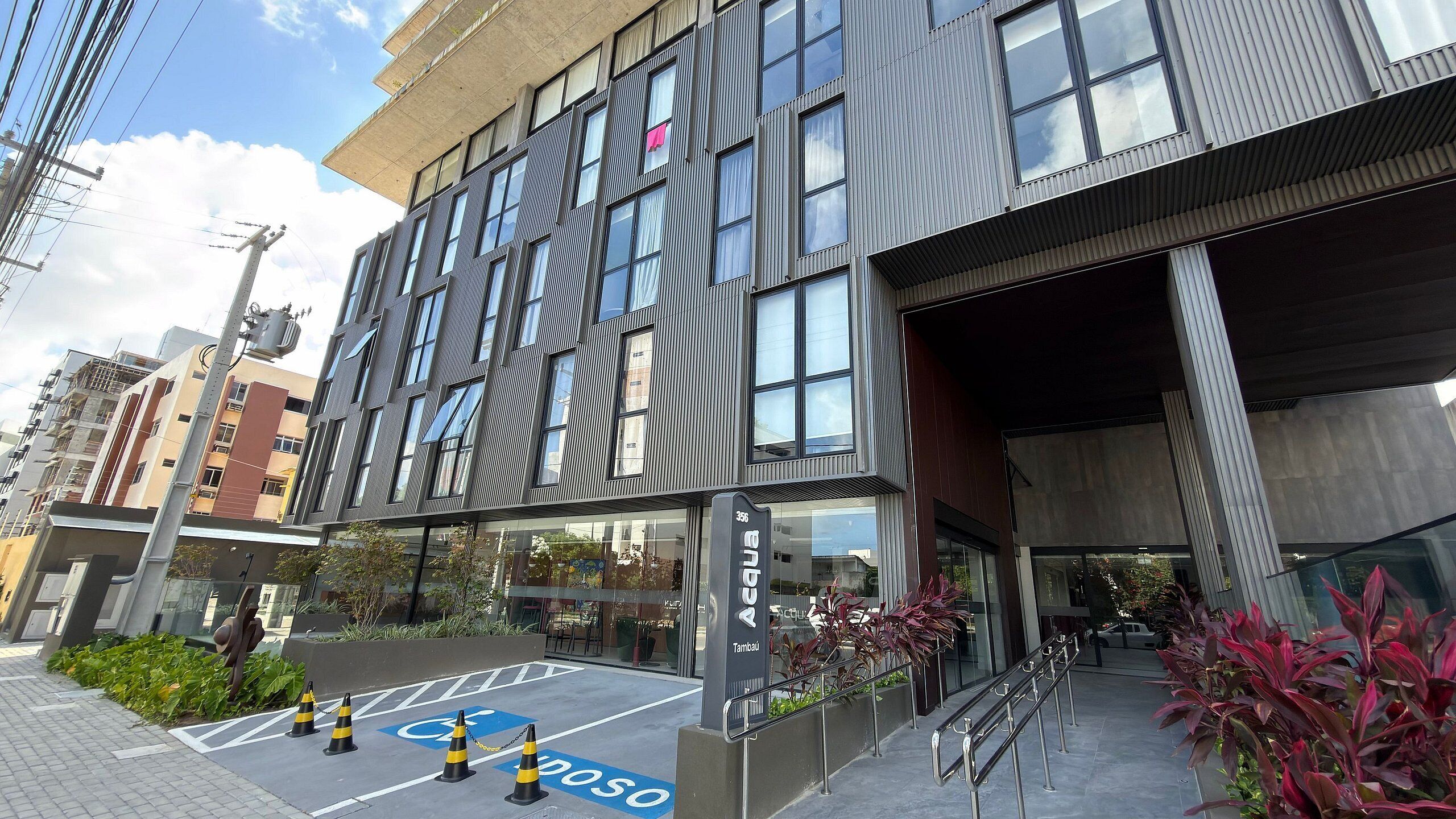 A modern building with a glass facade, a ramp leading to the entrance, and a parking area marked with a wheelchair symbol.