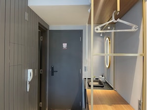 Ein modernes Hotelzimmer mit einer grauen Tür, einem Telefon, einem kleinen Waschbecken und einem hölzernen Ablagefach.