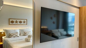 Ein Hotelzimmer mit einem Bett, einem großen Flachbildfernseher an der Wand, einem gerahmten Bild von Muscheln und Sternen sowie einer Holztür.