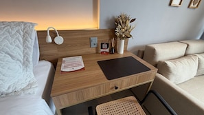 Habitación de hotel con cabecera de madera, mesita de noche con posavasos, jarrón con flores secas, cuadro enmarcado y un par de auriculares.