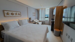 Una habitación de hotel moderna con una cama grande, un escritorio, una silla, un televisor y vistas a la ciudad.
