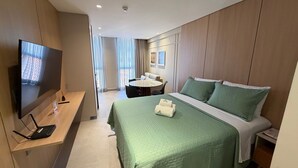 A hotel room with a bed, a TV, a desk, and a dining area. - Luxury flat fully equipped at Acqua Tambau AQ2X7 (João Pessoa)