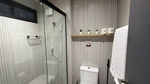Ein modernes Badezimmer mit einer Duschkabine aus Glas, einer Toilette und einem Ablagefach für Toilettenartikel.