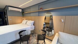 Une chambre moderne comprenant un lit, un bureau, des chaises, un miroir et une petite kitchenette.
