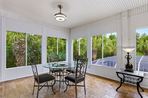Ein Zimmer mit Glastisch und Stühlen, großen Fenstern mit Blick ins Grüne und einem Deckenventilator.