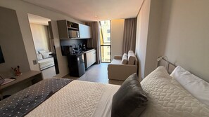 Ein Hotelzimmer mit Bett, Schreibtisch, Küchenzeile, Sofa und Blick ins Freie.