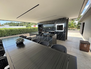 An outdoor patio with a dining table, chairs, and a grill area. - Apartment on the seafront of Cabo Branco UN204 (João Pessoa)