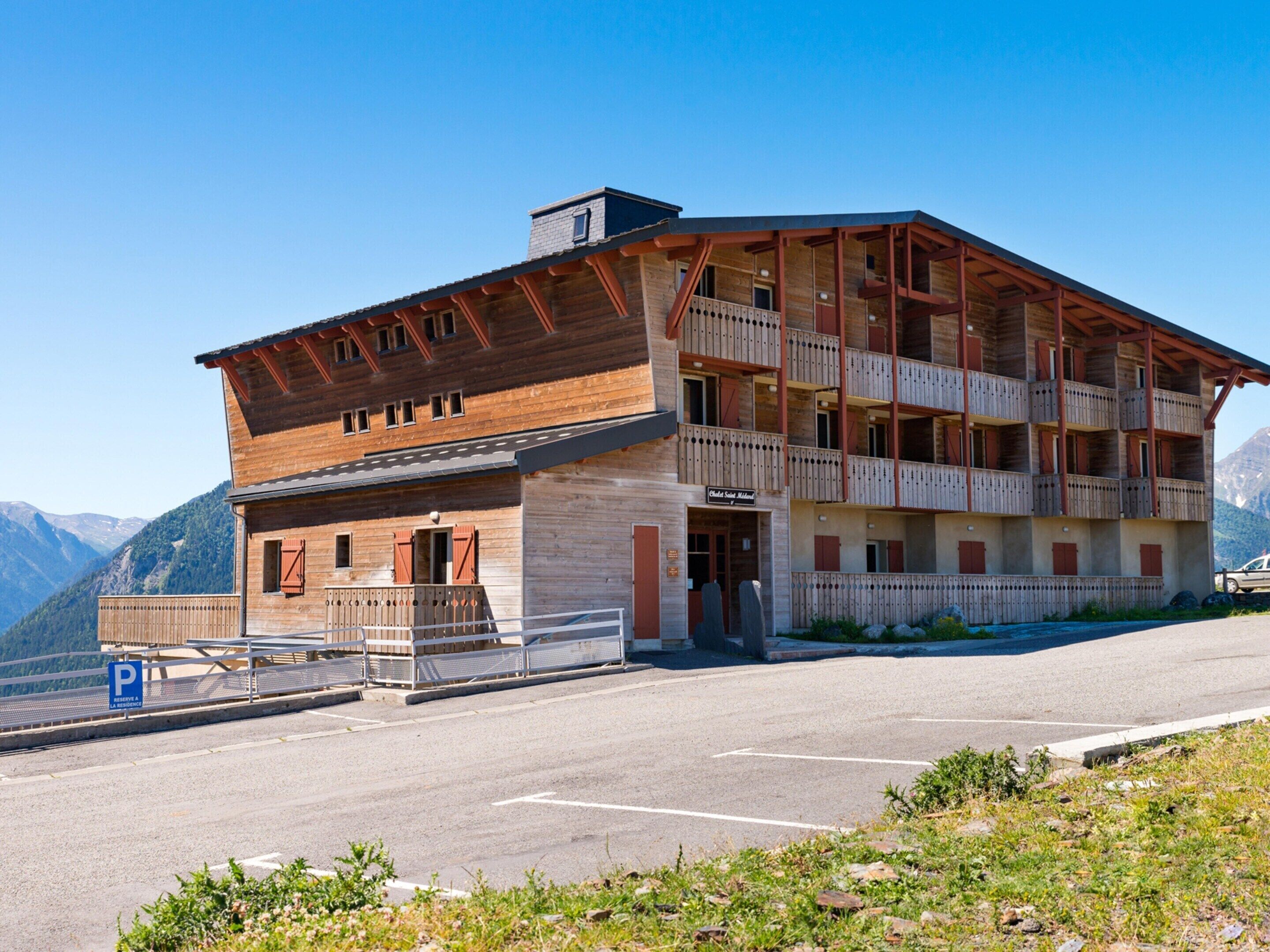 Un immeuble à plusieurs étages doté de balcons, d’un espace de stationnement et surplombant un paysage montagneux.