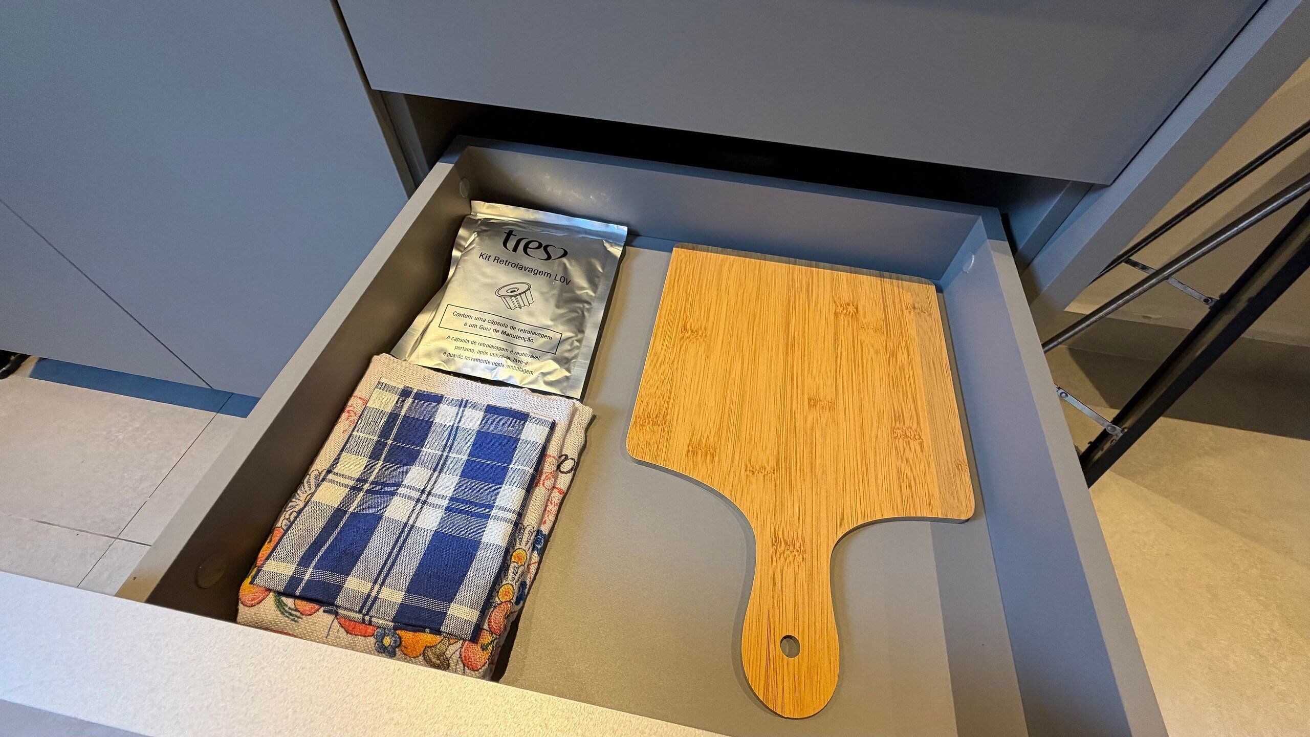 A drawer containing a wooden spatula, a packet of kitchen towels, and a fabric with a checkered pattern.