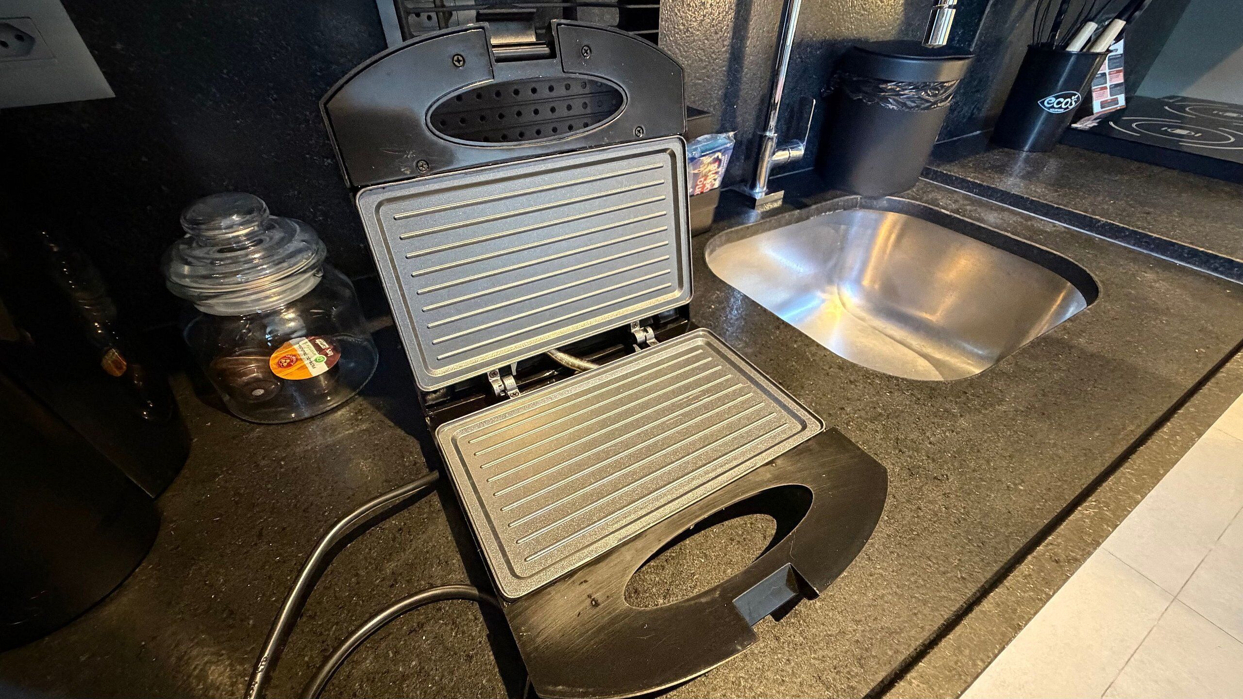 Una cocina con una plancha para gofres, un fregadero y una cafetera.