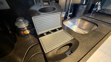 Una cocina con una plancha para gofres, un fregadero y una cafetera.