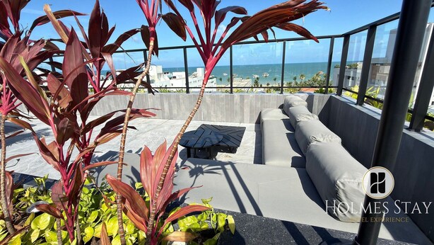 A rooftop terrace with a seating area, a view of the ocean, and a logo for Holmes Stay. - First floor apartment with terrace at Acqua Tambau AQTX3 (João Pessoa)