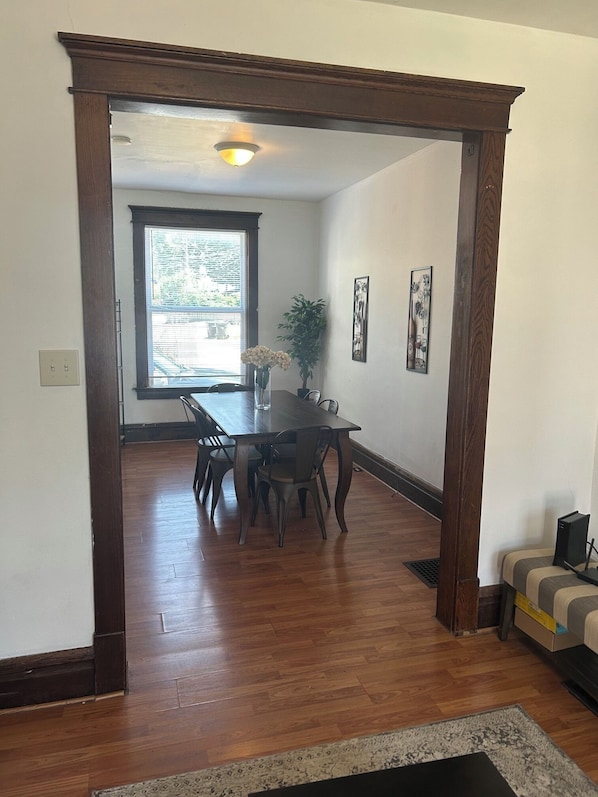 A dining area with a wooden table and chairs, a potted plant, and a window with blinds.